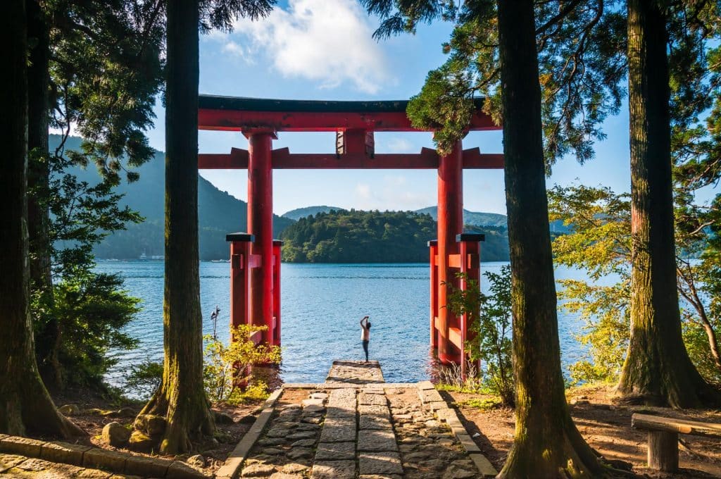 A Young Woman Takes Photos With Her Phone Of A Torii Gate In Hakone, Japan